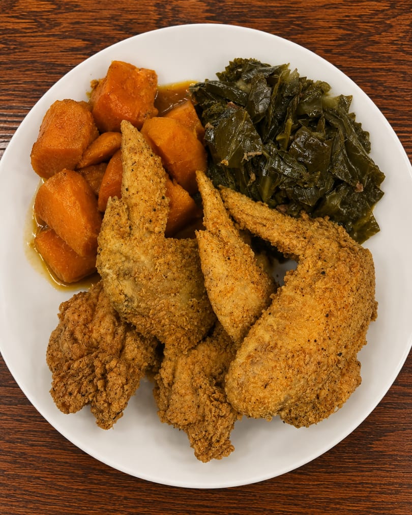 Fried chicken wings, candied yams, and collard greens on a white plate.