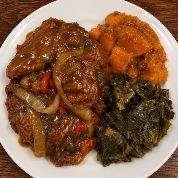 Smothered chicken with onions and peppers, candied yams, and collard greens on a white plate.